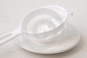 Icing sugar in a plastic sieve on top of white ceramic plate