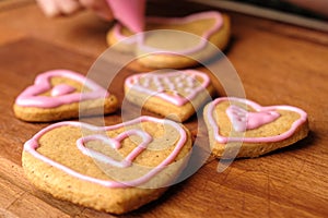 Icing of Valentines Day. Woman decorating gingerbread cookies in the shape of heart on a wooden table.