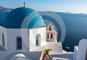 Iconic blue-domed church with pink bell tower and the Aegean Seain Greece