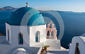 Iconic blue-domed church with pink bell tower and the Aegean Seain Greece