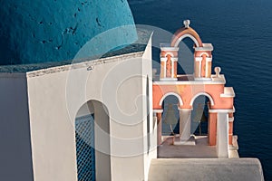 Iconic blue-domed church with pink bell tower and the Aegean Seain Greece