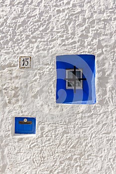 Iconic blue wooden window on white stone wall of typical Greek style house,