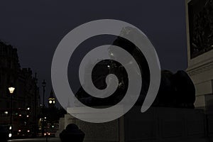 Iconic Lion Statue from Trafalgar Square with Big Ben in the Background during on overcast night concept for British Legacy,