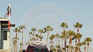 Iconic retro wooden lifeguard watch tower and baywatch red car. Life buoy, american state flag and palm trees against