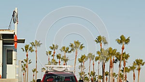 Iconic retro wooden lifeguard watch tower and baywatch red car. Life buoy, american state flag and palm trees against blue sky.