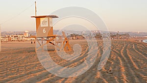 Iconic retro wooden orange lifeguard watch tower on sandy california pacific ocean beach illuminated by sunset rays