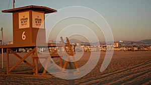 Iconic retro wooden orange lifeguard watch tower on sandy california pacific ocean beach illuminated by sunset rays