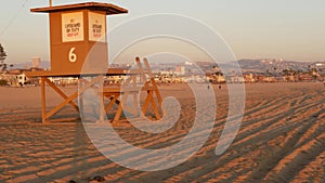 Iconic retro wooden orange lifeguard watch tower on sandy california pacific ocean beach illuminated by sunset rays. Private