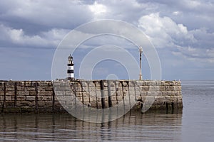 Iconic striped Seaham lighthouse on sea wall with cloud reflections