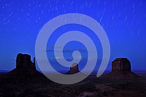 Iconic view of the three buttes of Monument Valley at night with star trails in the sky.. Stock picture