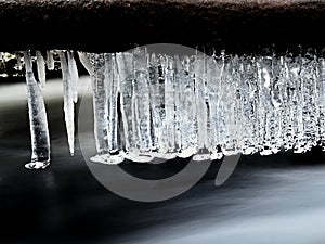 Icy branches above chilling stream. Reflections in icicles