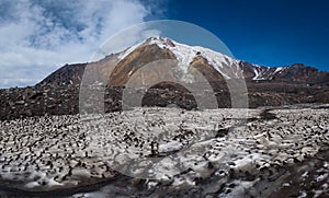 Icy glaciers on the slopes of Tolbachik Volcano viewed over a field with snow covered with sand and ash