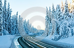 Icy highway through a forest with pine trees covered in heavy white snow