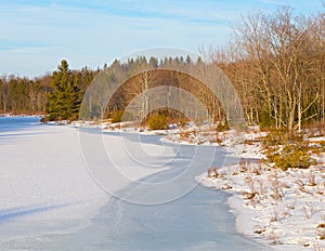 Icy pond in the woods at sunset.