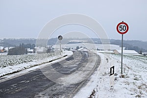 icy road into snowy village Welling in the valley, speed limit 50 sign on the hill already photo