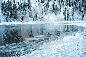 Icy shore of lake with snowy forest.