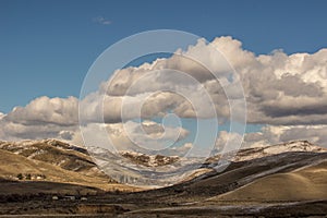 Idaho foot hills Ranch after a light snow under blue sky and broken clouds.