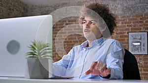 Idea coming to mind of nerd programmer with volume curly hair, working on laptop and sitting in modern office