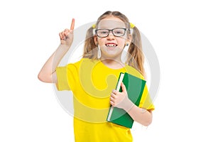 Idea. Points a finger up. Cheerful young child girl with glasses holding a book to study isolated on a white background.