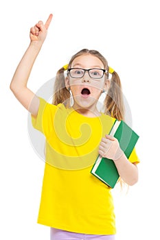 Idea. Points a finger up. Cheerful young child girl with glasses holding a book to study isolated on a white background.