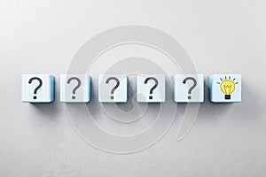 Idea and right solution concept with row of blue cubes with question mark and one with yellow light bulb on grey background