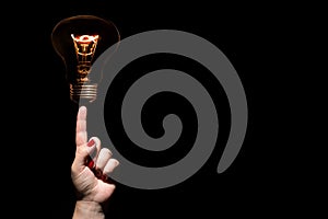 Idea and success coincept. Glowing light bulb without wires on female hand with trigger finger and red nails on black background.