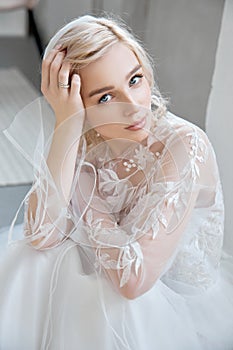 Ideal bride sitting on the floor, portrait of a girl in a long white dress. Beautiful hair and clean, soft skin. Wedding hairstyle