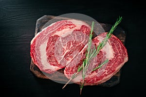 Ideal raw rib eye beef steak with rosemary on black wooden background