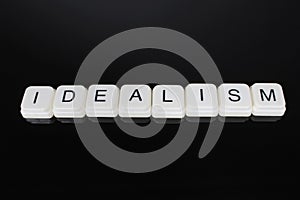 Idealism text word title caption label cover backdrop background. Alphabet letter toy blocks on black reflective photo