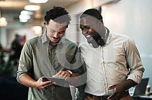 Ideas are better shared. two young businessmen standing together in the office and using a digital tablet.