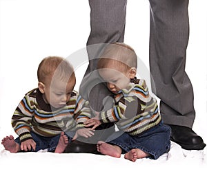 Identical twin baby boys holding dads legs photo