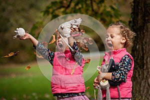 Identical twins having fun with autumn leaves, blond cute curly girls, happy family, beautiful girls in pink jackets