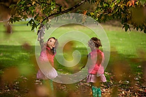 Identical twins having fun with autumn leaves, blond cute curly girls, happy family, beautiful girls in pink jackets