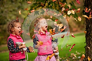 Identical twins having fun with autumn leaves, blond cute curly girls, happy family, beautiful girls in pink jackets