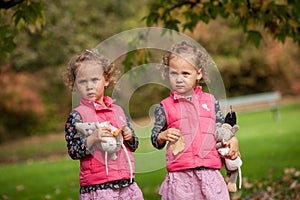 Identical twins having fun with autumn leaves, blond cute curly girls, happy family, beautiful girls in pink jackets