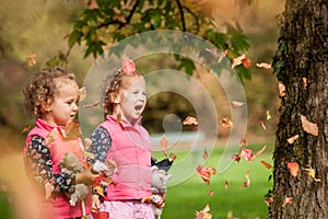 Identical twins having fun with autumn leaves, blond cute curly girls, happy family, beautiful girls in pink jackets