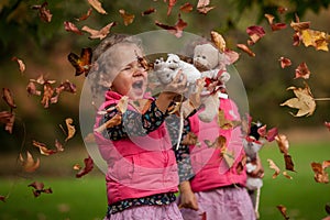 Identical twins having fun with autumn leaves, blond cute curly girls, happy family, beautiful girls in pink jackets