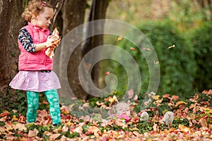Identical twins having fun with autumn leaves in the park, blond cute curly girls, happy kids, beautiful girls in pink jackets