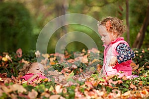 Identical twins having fun with autumn leaves in the park, blond cute curly girls, happy kids, beautiful girls in pink jackets