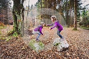 Identical twins are jumping from rocks in forest on hiking.