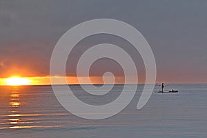 Idilic reddish sunset. Fisherman over raft on sea