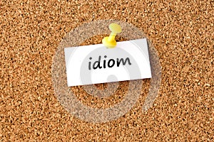 Idiom. Word written on a piece of paper, cork board background