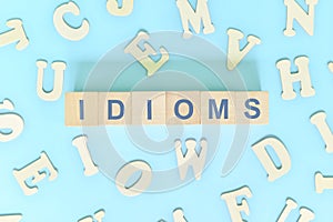 Idioms or idiom concept in English grammar class lesson. Wooden blocks typography flat lay in blue background.