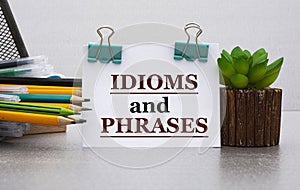 IDIOMS and PHRASES - words on a white sheet with clamps against the background of a cactus and jars with pencils