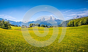 Idyllic alpine landscape with green meadows, farmhouses and snow-capped mountain tops