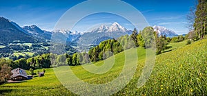 Idyllic alpine landscape with green meadows, farmhouses and snow-capped mountain tops