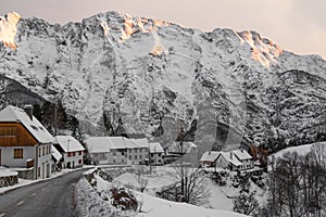 Idyllic alpine snowy mountain pass road through village in sunset sky, Julian Alps, Slovenia