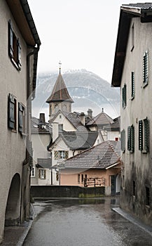 Idyllic alpine village in Switzerland with a vlilage road leading through old building and many roofs in the background