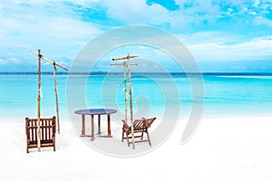 Idyllic beach in the Maldives with two wooden chairs and a table situated on the sand