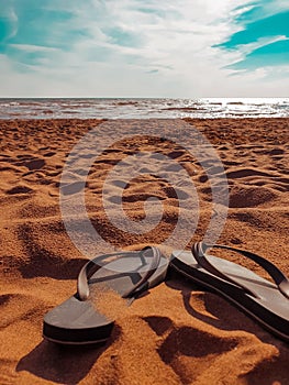 Idyllic beachscape featuring a pair of aqua blue sandals in the sand with a clear blue sky and ocean